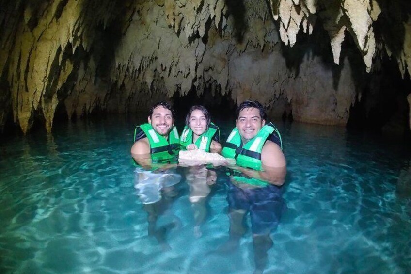 Three people in a cave with clear water, wearing life vests. 4