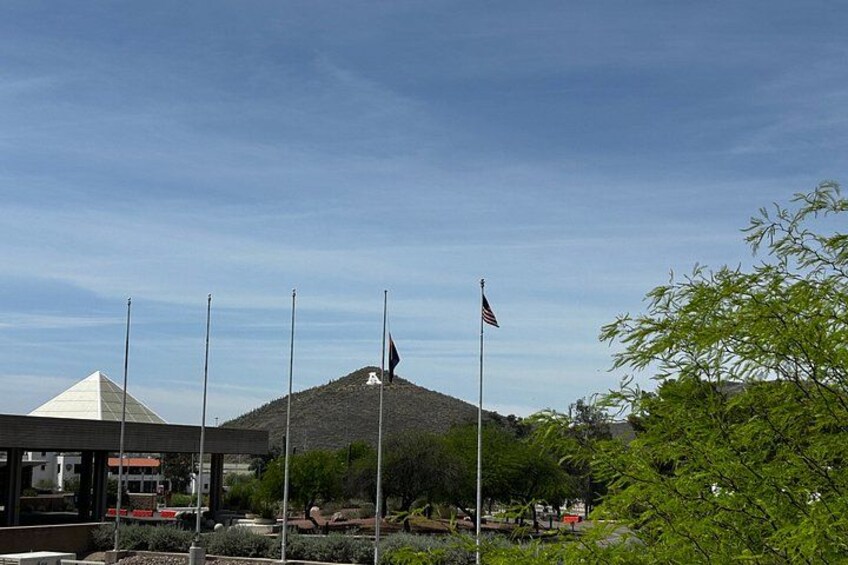 A building with a pyramid-shaped roof, multiple flagpoles, and a hill in the background. 3