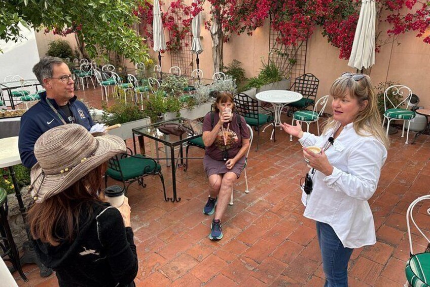 A group of people sitting at outdoor tables in a patio area with chairs and umbrellas. 1