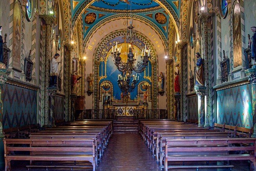 An ornate church interior with pews, a central altar, and detailed wall decorations. 2