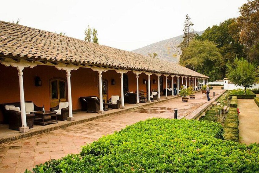 A covered outdoor seating area with chairs and tables, surrounded by a garden with neatly trimmed bushes. 3
