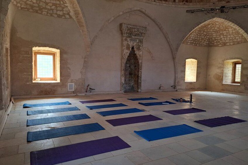 An interior with stone arches, a central arched niche, and mats arranged on the floor. 2