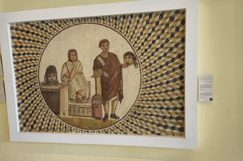 A mosaic with three figures, one standing and two seated, surrounded by a patterned border. 1