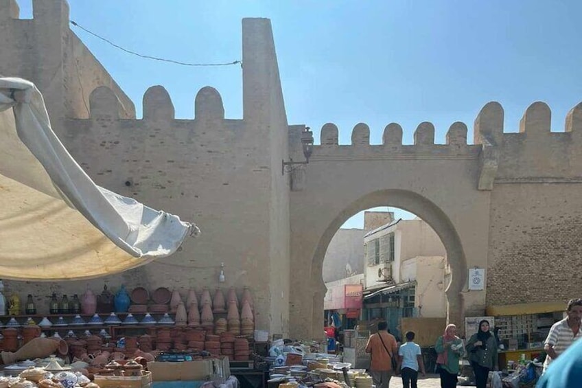 A market with a large archway, various stalls, and a historic wall. 3