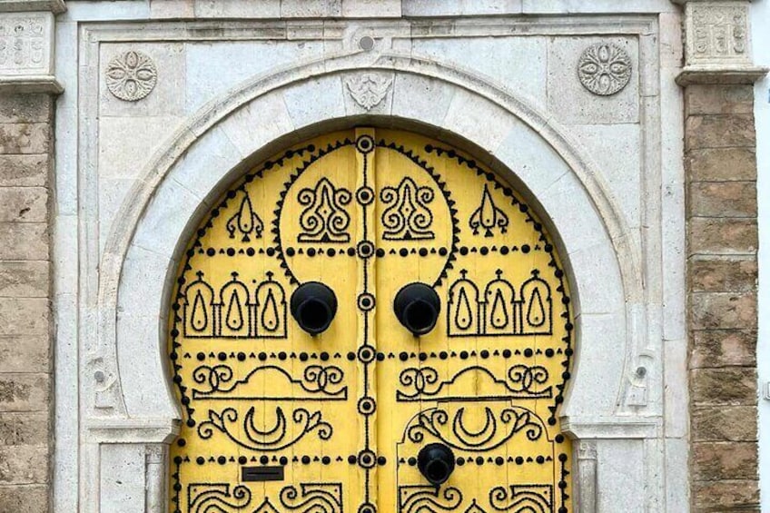 A yellow door with black designs and two round black handles, set within an arched stone frame. 2