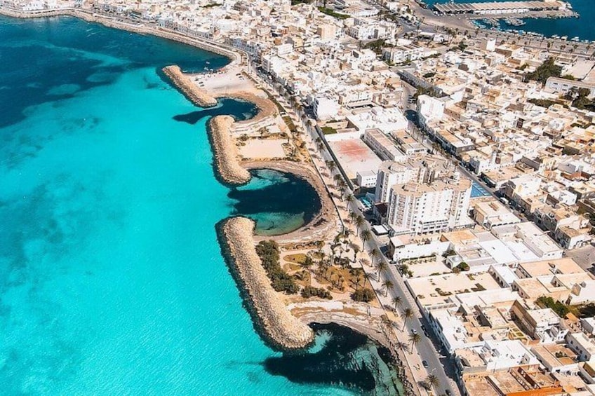 An aerial view of a coastal city with a clear blue sea, a fortified harbor, and densely packed buildings. 5