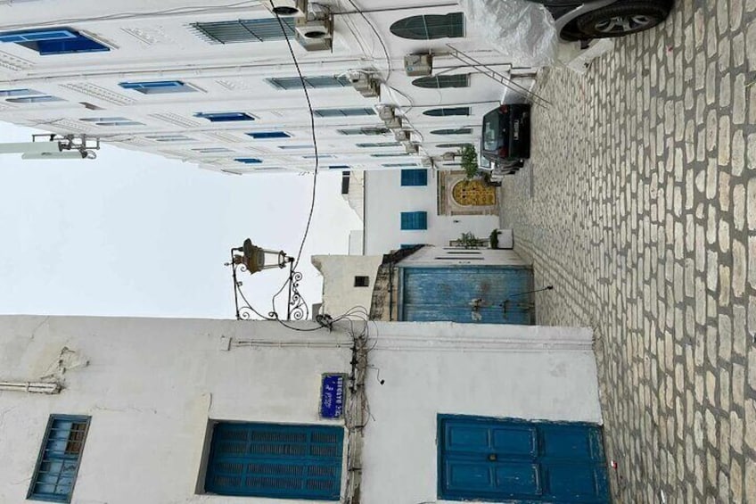 A narrow street with white buildings, blue doors, and a tiled roof. 4