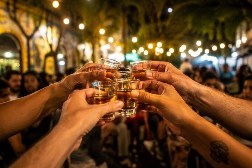 A group of people toasting with drinks in a crowded indoor setting with string lights. 1
