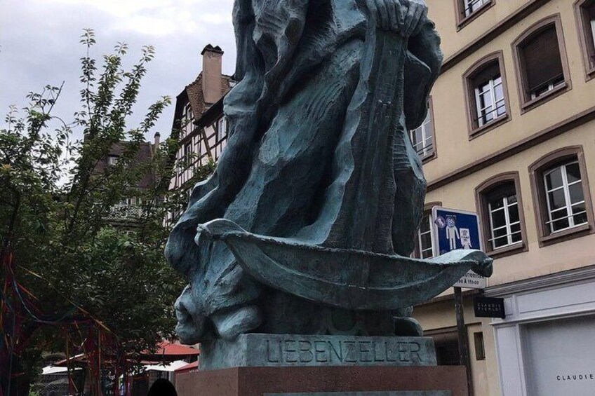 A statue of a woman with a flowing dress, labeled 'LIEBZELLER,' in an urban setting with buildings and a signboard in the background. 4