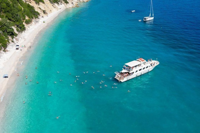 A beach with clear turquoise waters, a white boat with people on board, and a sailboat in the distance. 3