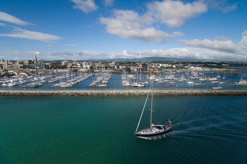 A marina with numerous sailboats docked, a single sailboat in motion, and a cityscape in the background. 1