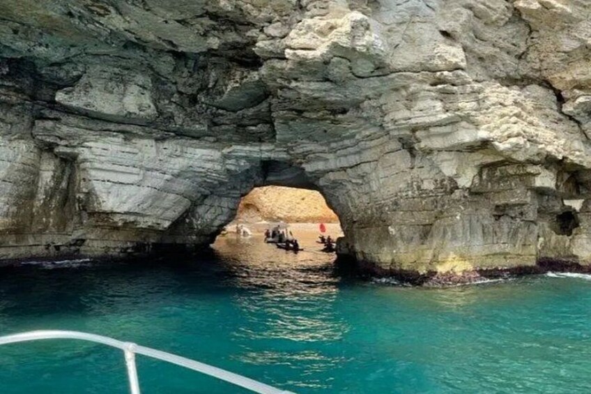 A natural rock formation with a cave-like opening, clear blue water, and a boat in the foreground. 4