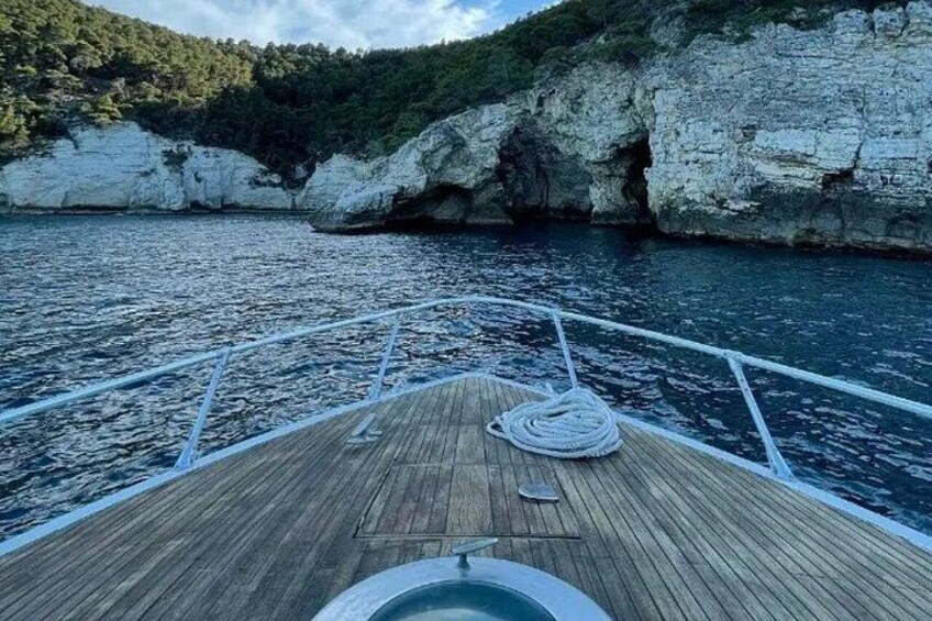 A wooden boat deck with ropes and a circular object, rocky cliffs, and a calm sea. 5