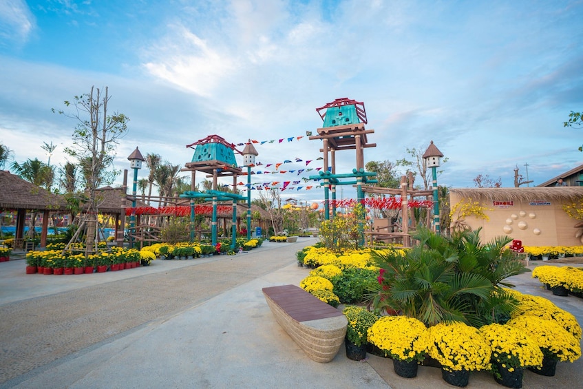 A theme park with colorful buildings, a pathway lined with yellow flowers, and a clear sky. 4