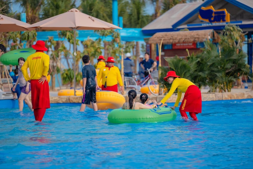 Lifeguards in yellow and red uniforms assisting people on inflatable tubes in a pool. 3