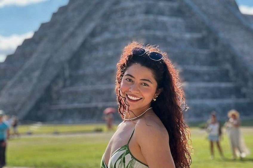 A person in a green dress with sunglasses on their head, standing in front of a large pyramid-like structure. 3