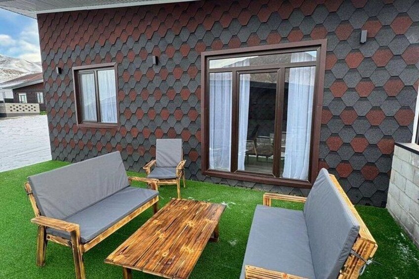 Et moderne hus med en hexagonal facade, en træterrasse og udendørs møbler. 2