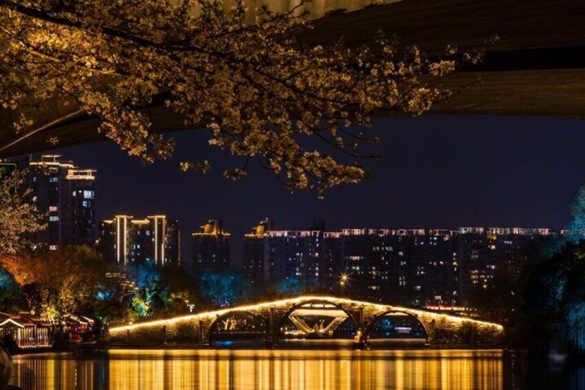 A nighttime cityscape with illuminated buildings and a bridge with decorative lights. 5