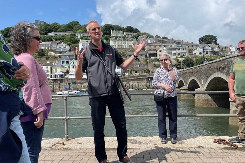 A group of people standing by a waterfront with a stone bridge in the background. 3