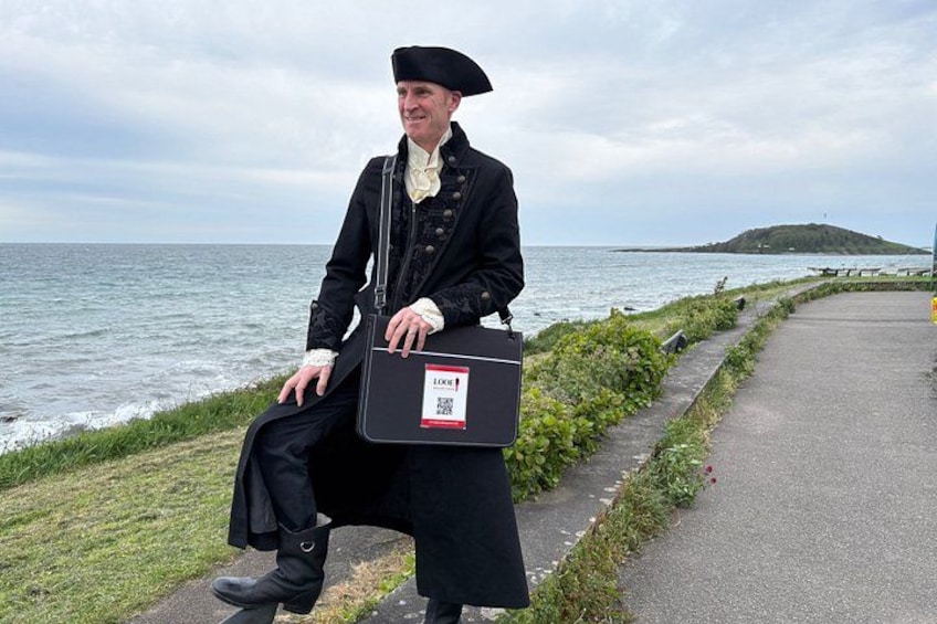 A person in historical attire sitting by the sea, holding a briefcase. 1