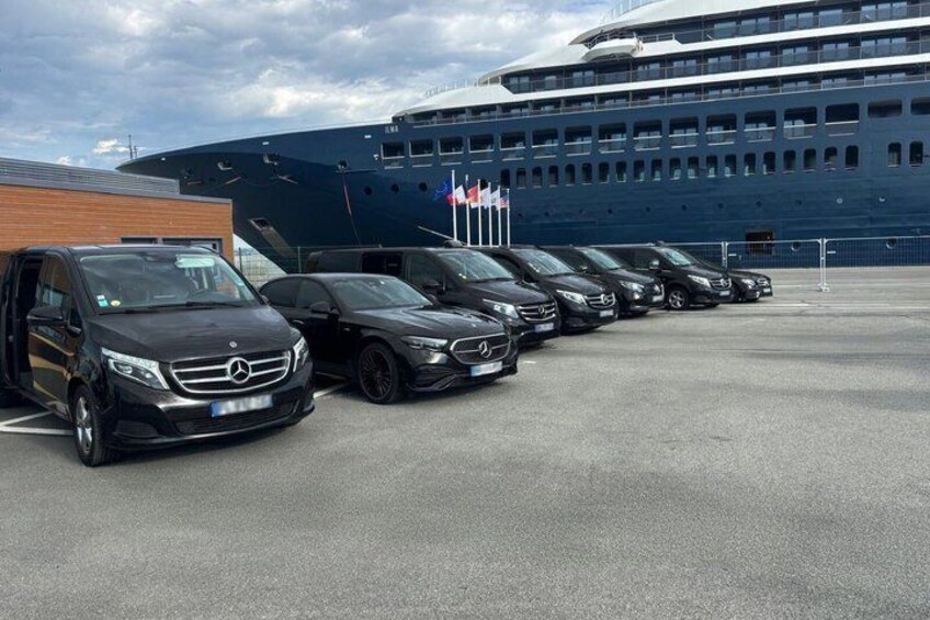 A row of parked cars in front of a large cruise ship. 2