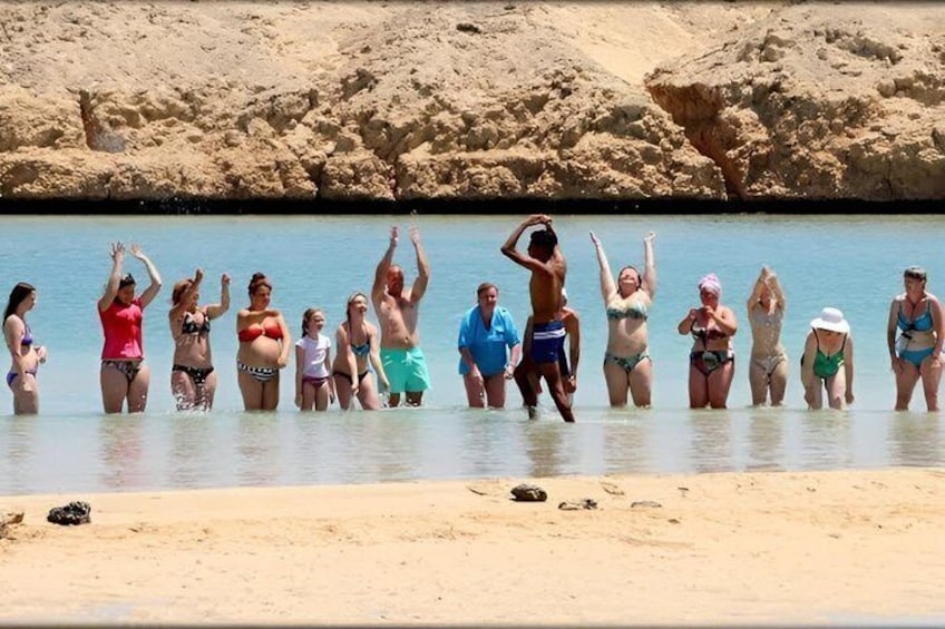 A group of people standing in shallow water at a beach with rocky cliffs in the background. 2