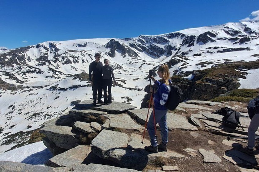 A group of hikers on a rocky mountain peak with snow-covered slopes in the background. 5
