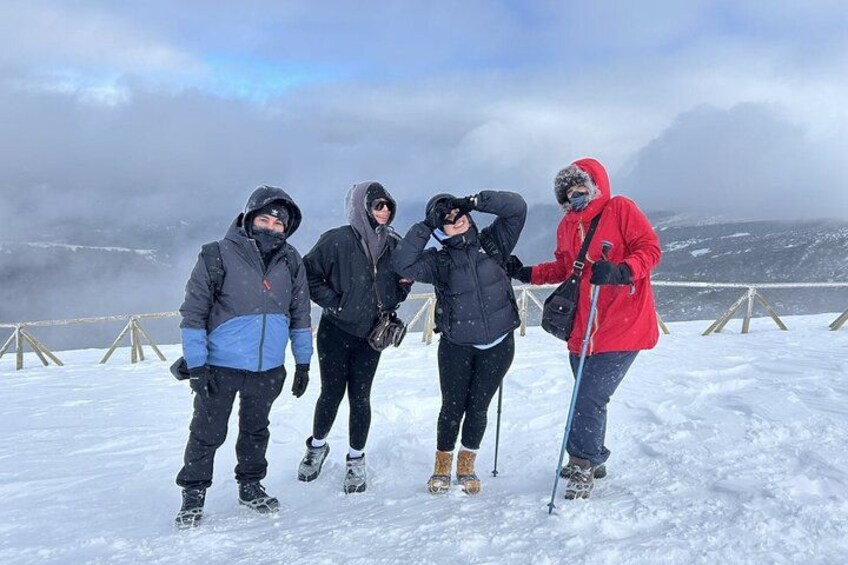 Four people standing on a snowy mountain with a cloudy sky in the background. 2
