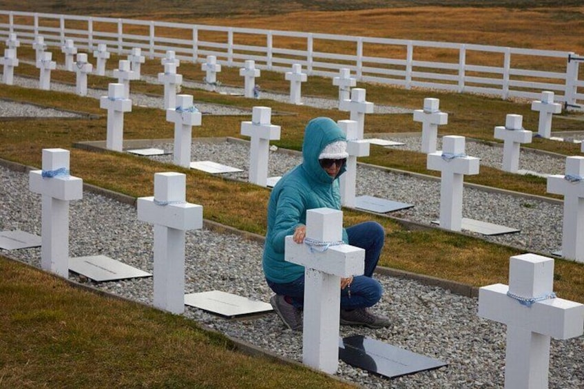 A person crouching in a cemetery with white crosses and headstones. 2