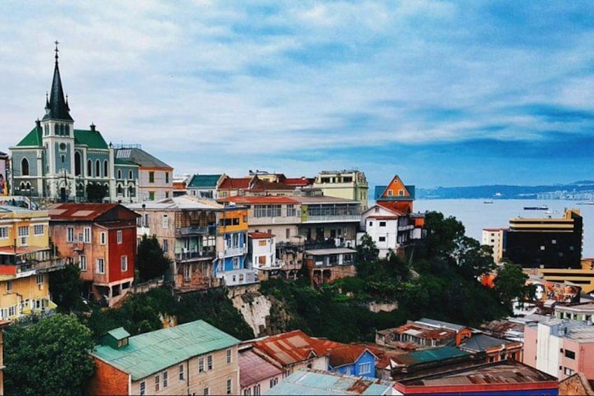 A coastal cityscape with colorful buildings, a prominent church with a green roof, and a body of water in the background. 1