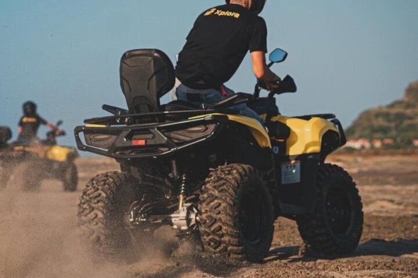 Iemand rijdt op een gele quad over een zandpad, met nog een quad op de achtergrond. 1