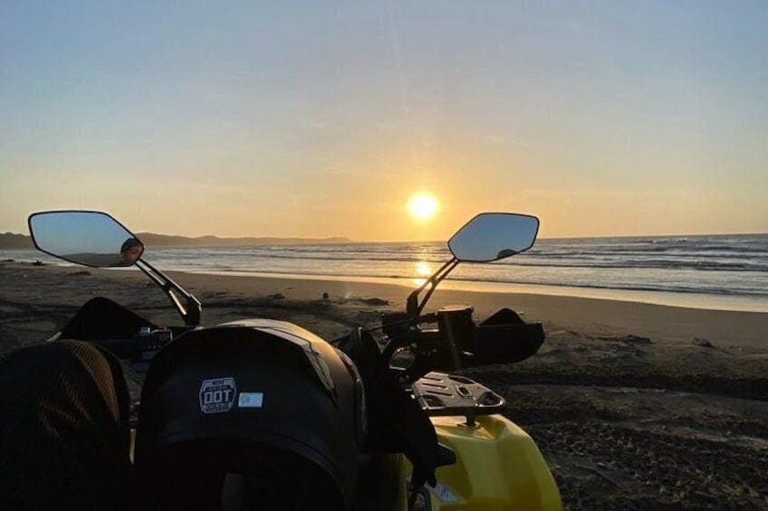 Een motorfiets geparkeerd op het strand, met een ondergaande zon op de achtergrond. 5
