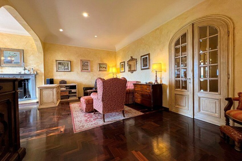 A room with a patterned armchair, a wooden cabinet, a fireplace, and a large arched doorway. 2