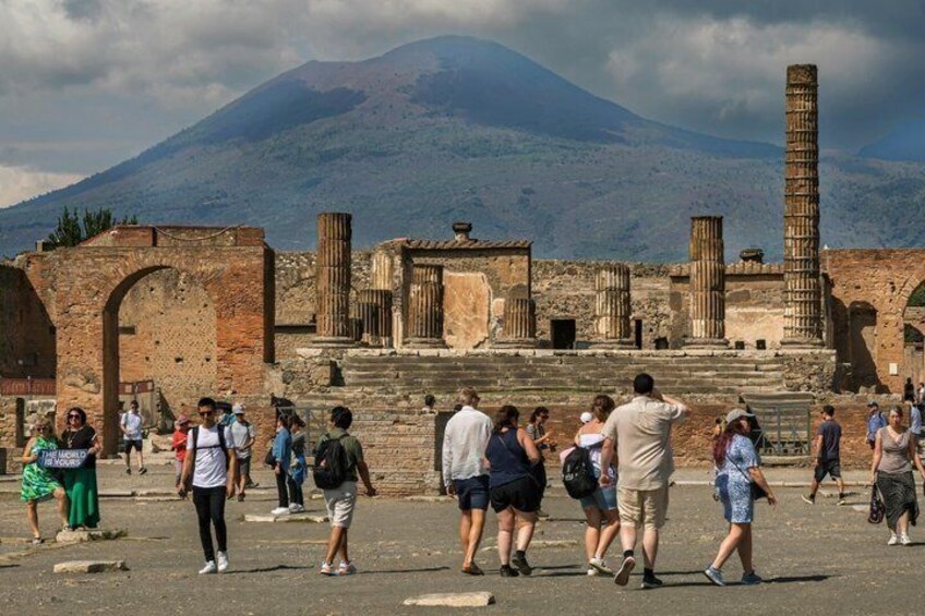 Ancient ruins with tourists, a mountain in the background, and a tall column. 1