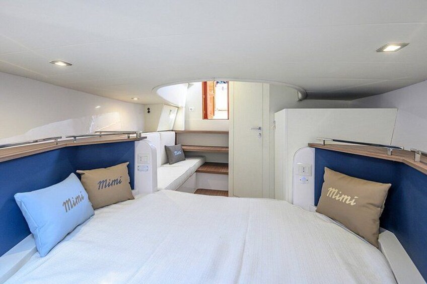 A compact, well-lit cabin with a bed, two pillows, a small seating area, and a kitchenette. 3