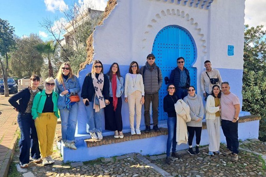 A group of people standing in front of a building with a blue door and white walls. 2