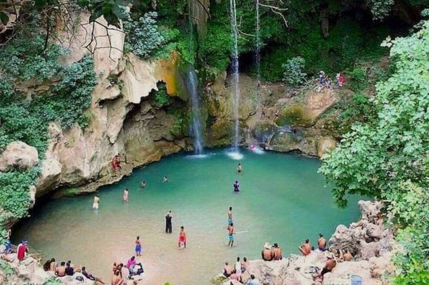 A natural pool with people swimming and relaxing, surrounded by rocks and greenery. 3
