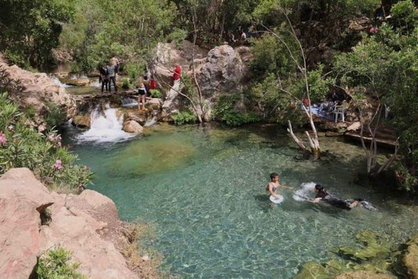 A clear water body with people swimming and a waterfall. 5