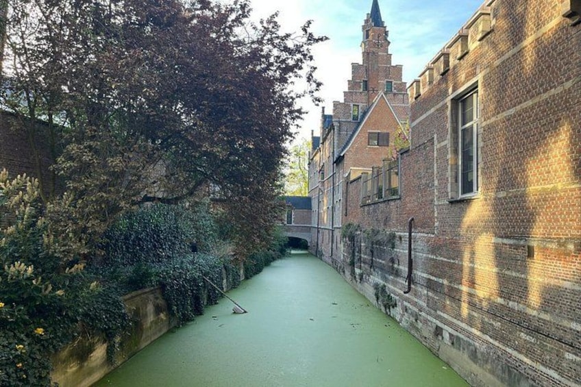 A narrow canal with a brick building on one side and a tree-lined path on the other. 5