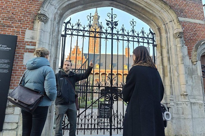 A wrought iron gate with a statue in the background, a brick building, and a person pointing at the gate. 1