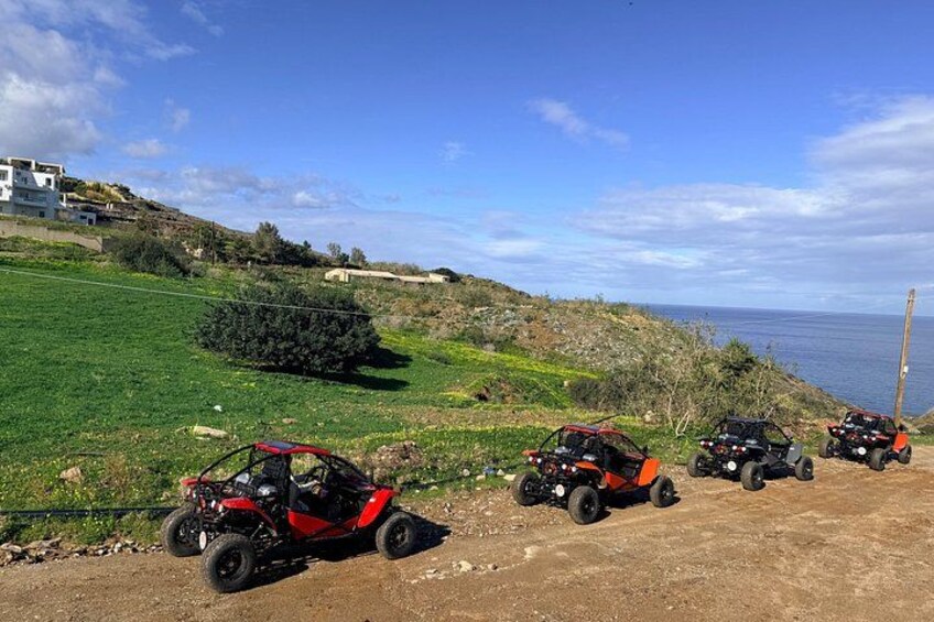 Off-road vehicles parked on a dirt path near a coastal area with greenery and a clear sky. 2