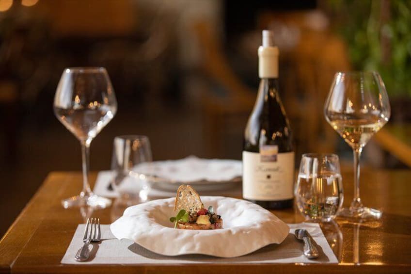 A dining table with a plate of food, a bottle of wine, and two wine glasses. 3