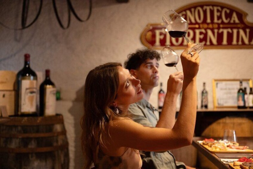 Two people holding wine glasses in a bar with a sign that reads 'ENOTECIA FIORENTINA.' 4