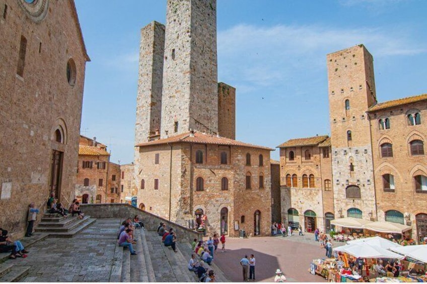 A historic square with stone buildings, a central staircase, and outdoor market stalls. 3