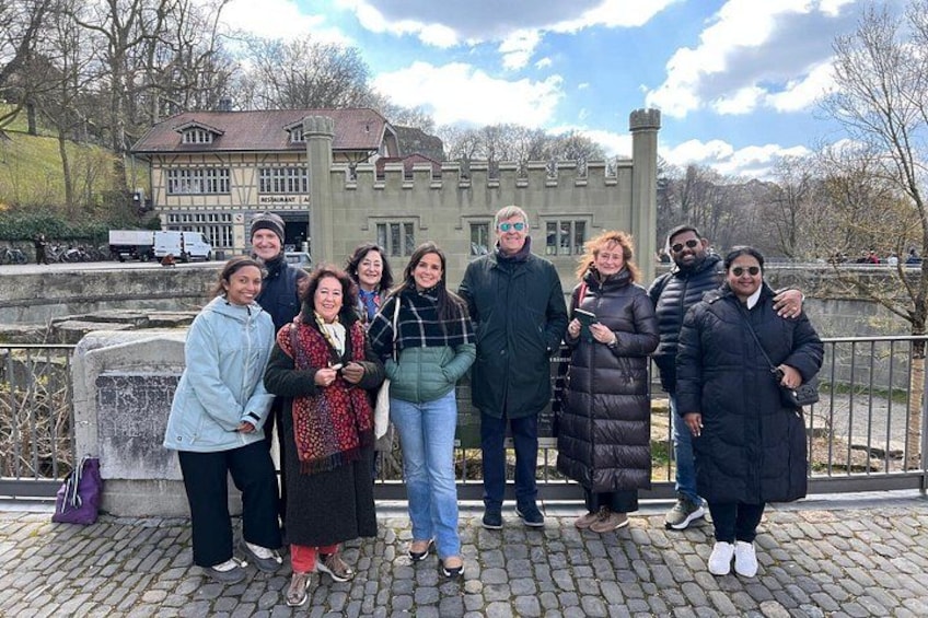 A group of people standing in front of a castle-like building with a stone wall and a paved area. 4