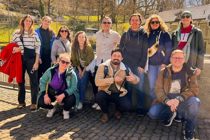 A group of people posing for a photo in an outdoor setting with cobblestone pavement and trees in the background. 3