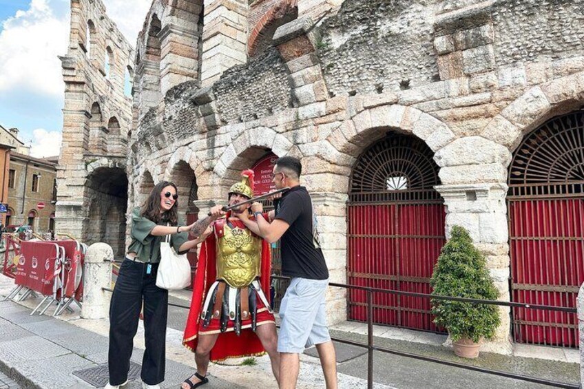 A person in a golden helmet and red cape posing with others in front of a historic stone building with arched windows and red doors. 1