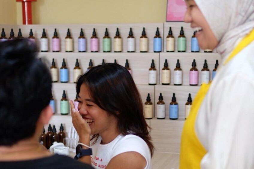A person in a white shirt and yellow apron, likely a staff member, in a setting with multiple small bottles on shelves in the background. 3
