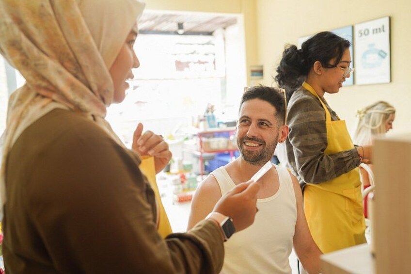 A person in a white tank top and yellow apron standing at a counter, possibly in a cafe or small shop. 5