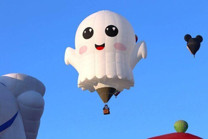 A white ghost-shaped hot air balloon with a smiling face, a smaller black balloon, and a green watermelon. 3